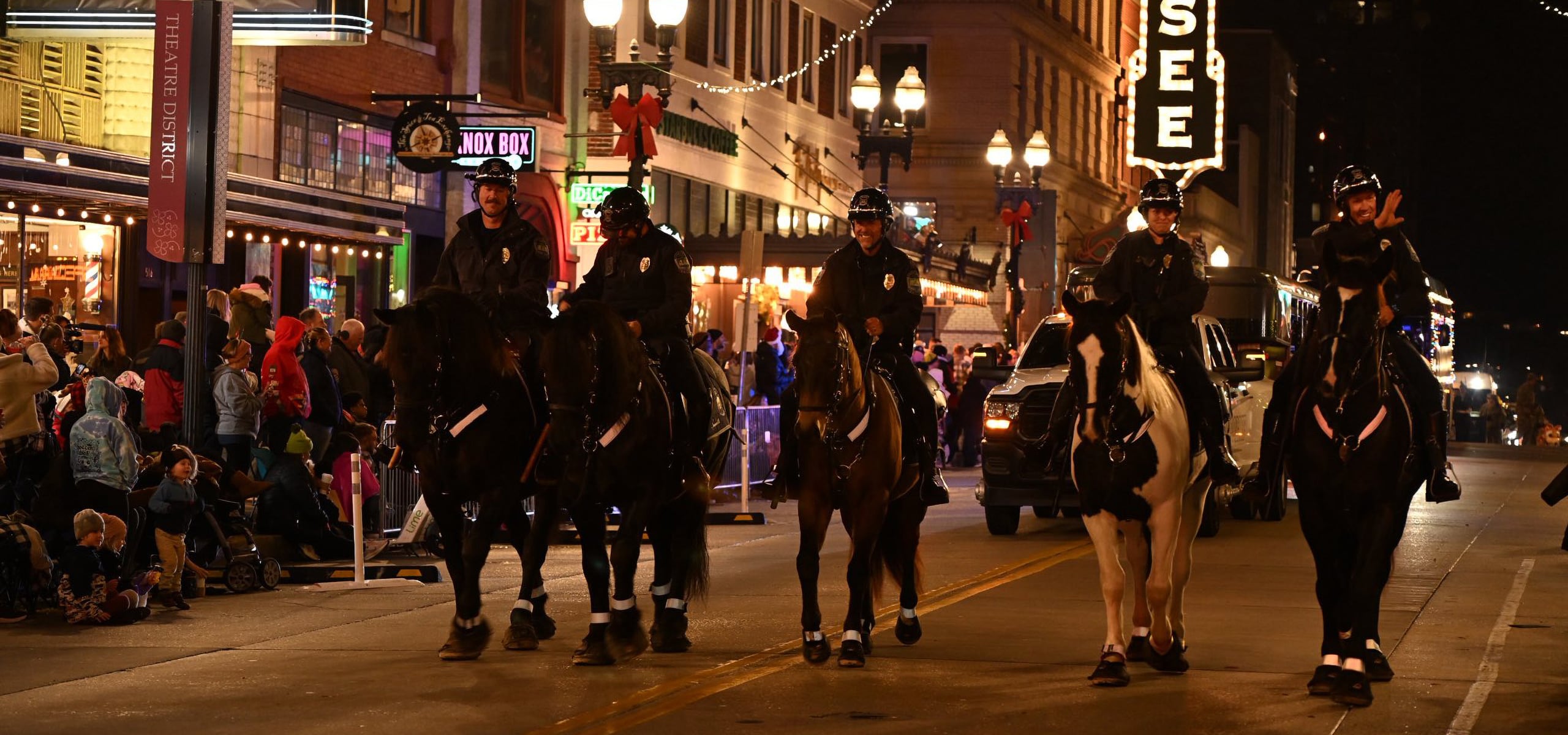 A group of mounted police officers in a parade at night, with a crowd in the background